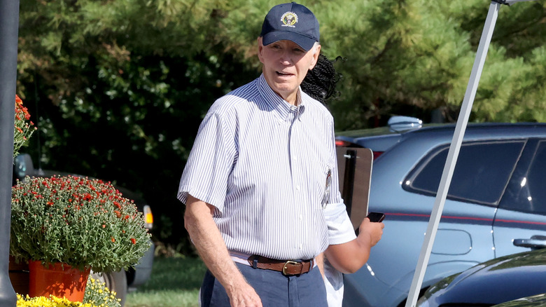 Joe Biden smiling while walking in a light blue check shirt and a navy baseball cap