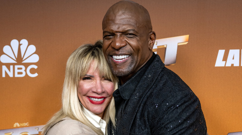 Rebecc and Terry Crews smiling while and embracing while posing together