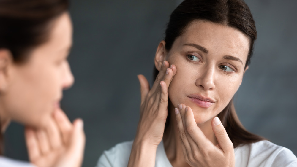 Woman looks at her dry skin in the mirror