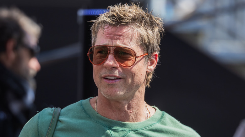 Brad Pitt smiling while wearing sunglasses and a light green T-shirt, with a bag on his shoulder