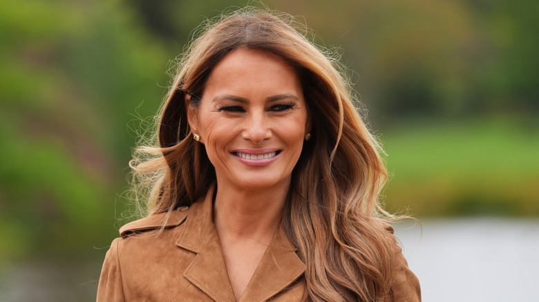 Melania Trump smiling in a brown jacket with her hair loose