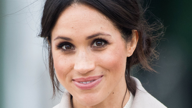 Meghan Markle with her hair pulled into a low bun smiling for a picture