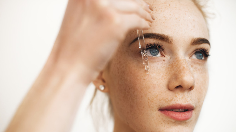 woman applying serum to her cheek while looking upward