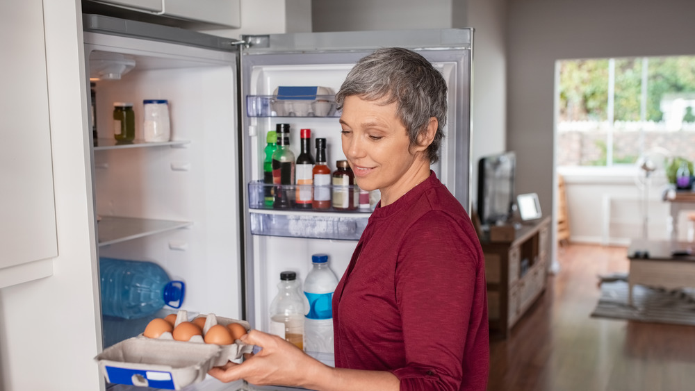 A woman smiling while removing eggs from the fridge 