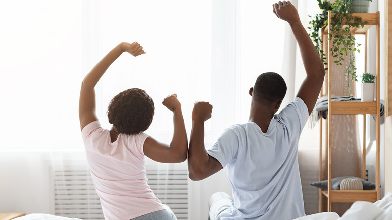 couple waking up in morning, sitting on bed and stretching