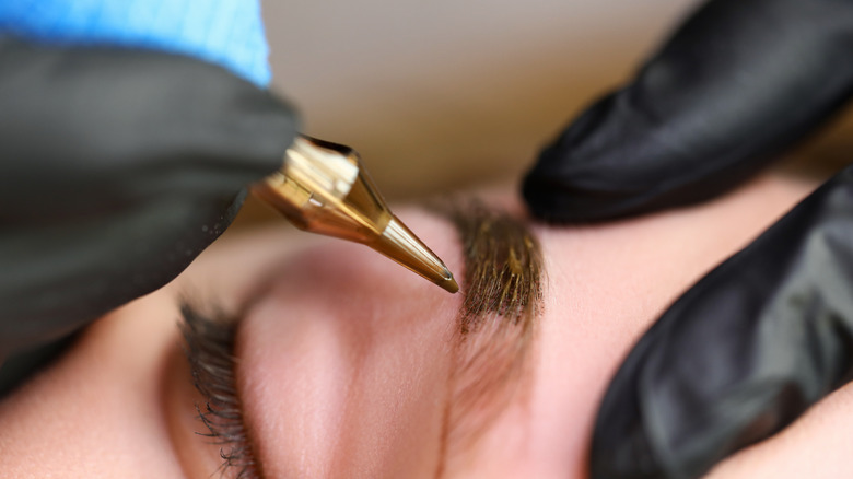 Microblading tool against woman's eyebrow