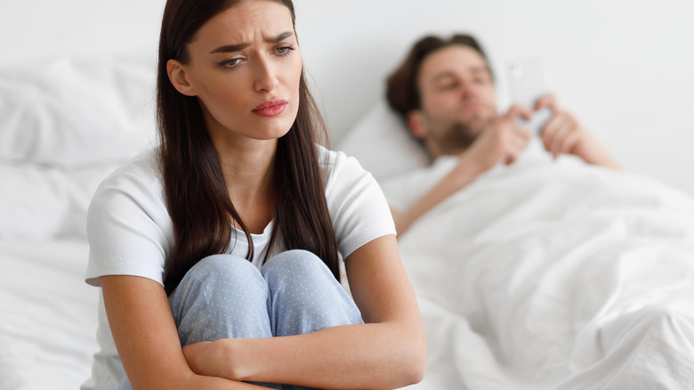 Unhappy woman sitting while man texts