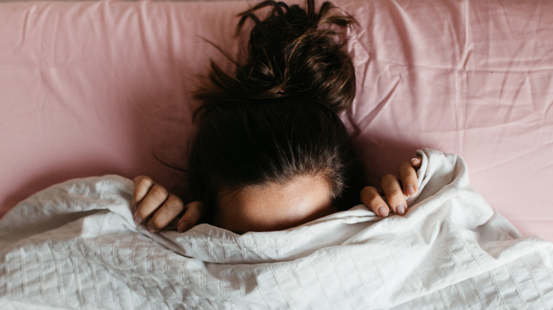 Woman laying on sheets and hiding her head