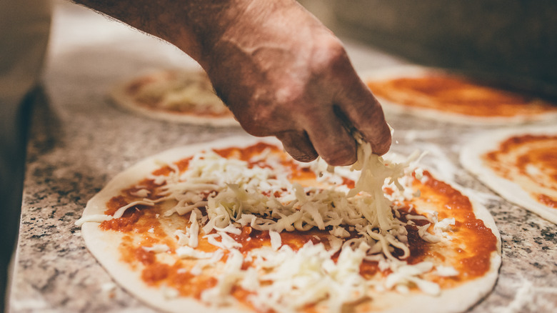 hand spreading cheese on pizza