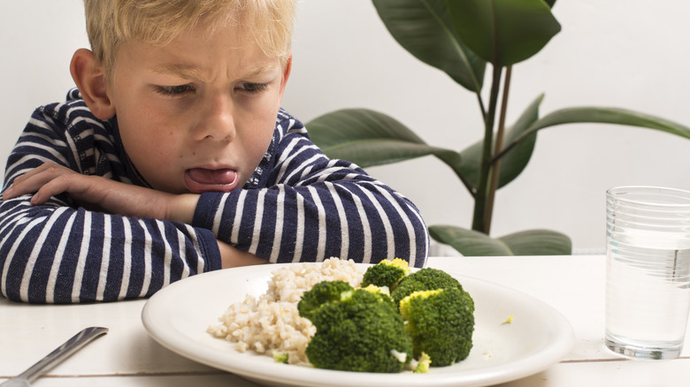 Child making an angry face while looking at veggies