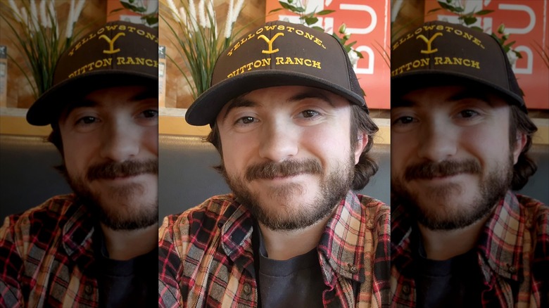 Close-up of Atticus Shaffer wearing "Yellowstone Dutton Ranch" cap and smiling