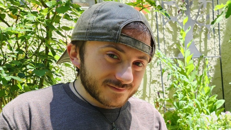 Close-up of Atticus Shaffer wearing backwards cap and surrounded by greenery outside