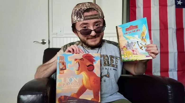 Atticus Shaffer sitting in chair and posing with two "The Lion Guard" books