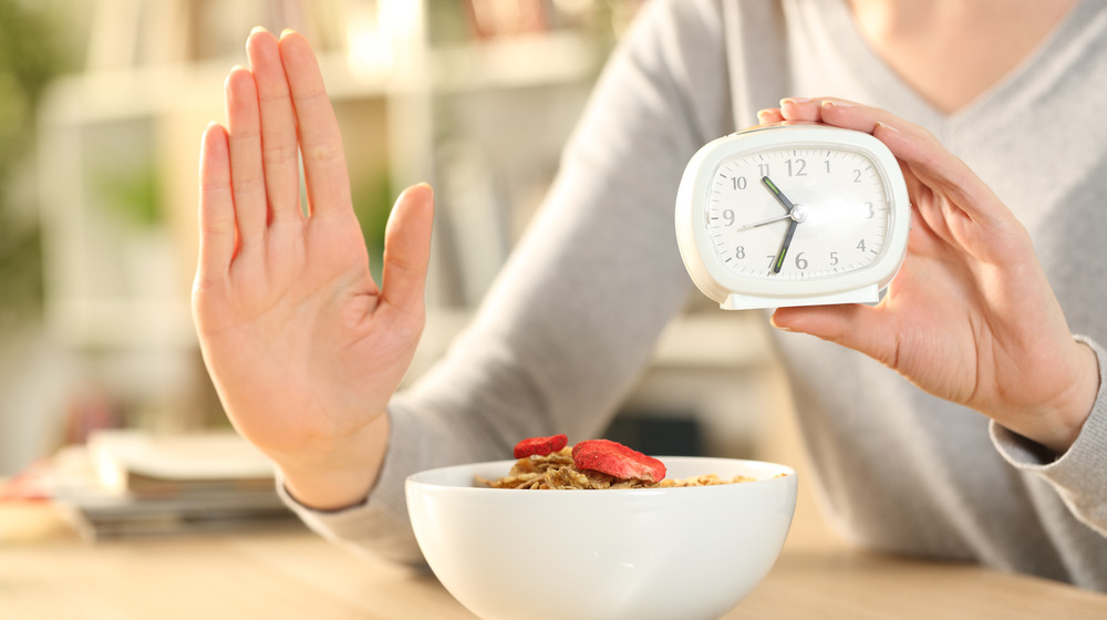 Woman holding an alarm clock with her hand out over a bowl of cereal.