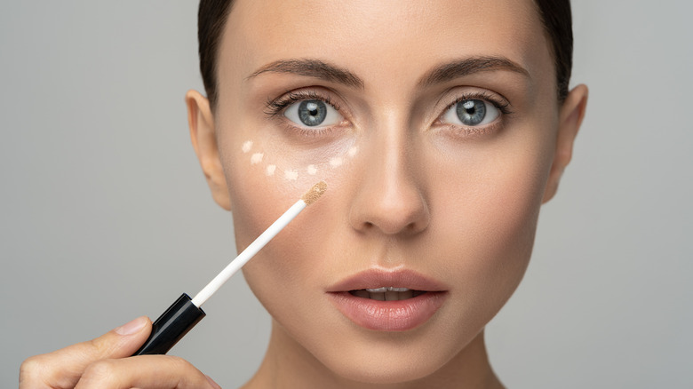 Woman applying concealer under her eyes