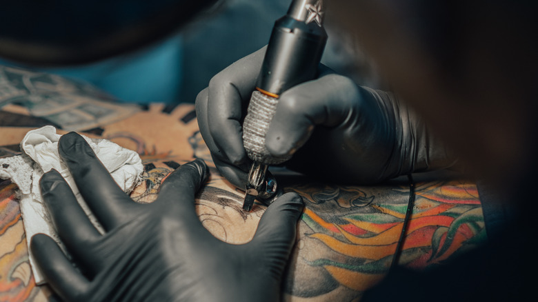 Closeup of tattoo artist wearing gloves and holding equipment tattooing someone's back