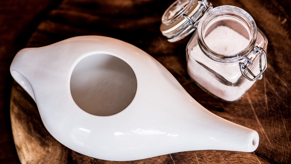 White Neti pot next to a jar of salt