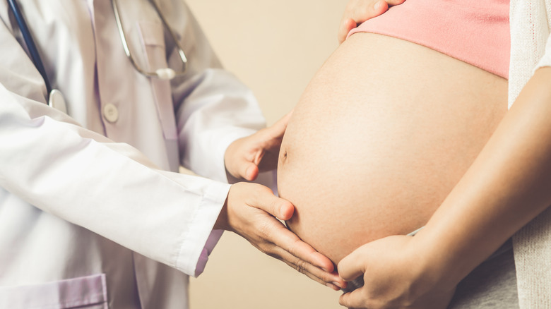 Doctor examining woman's pregnant belly