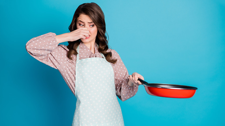 Woman holding up a pan as she holds her nose