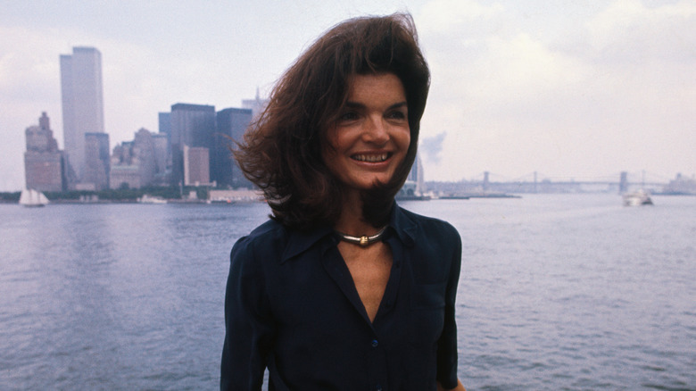 Jackie Kennedy smiling as her hair blows in the wind and New York Harbor and skyline in the background