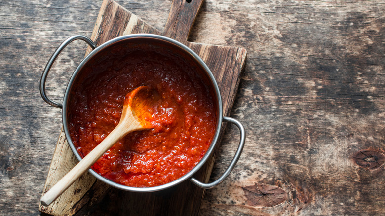 A pot of red sauce on a cutting board