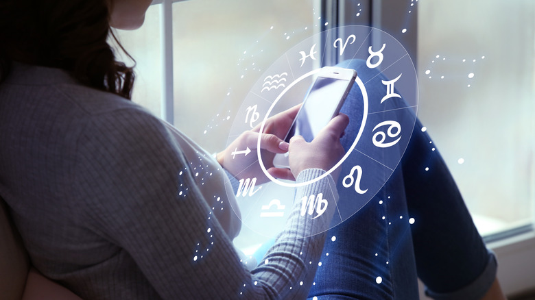 Woman holding phone with zodiac circle surrounding it