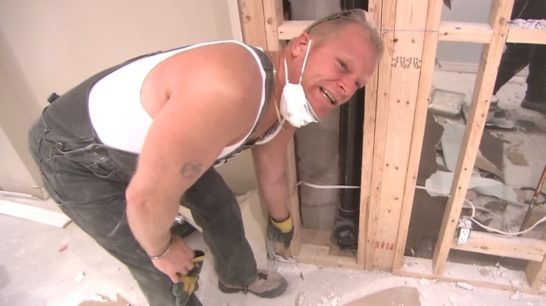 Mike Holmes bending down in construction site pointing at shoddy work