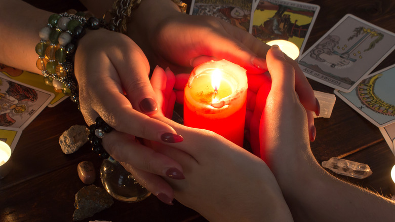 Woman holding hands with fortune teller around lit candle