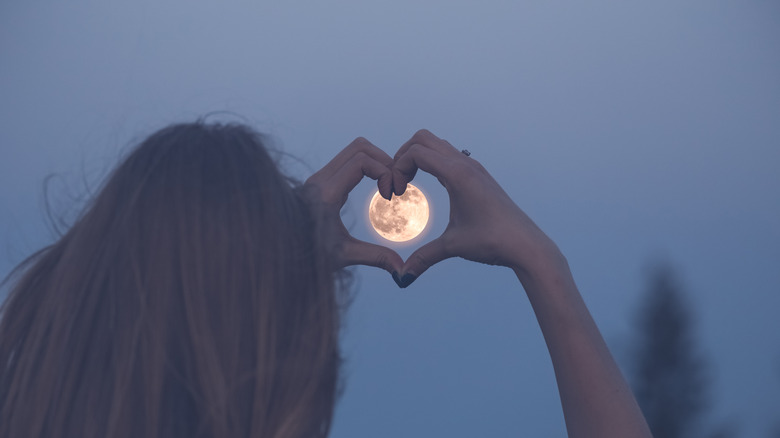 person making heart shape with hands over moon