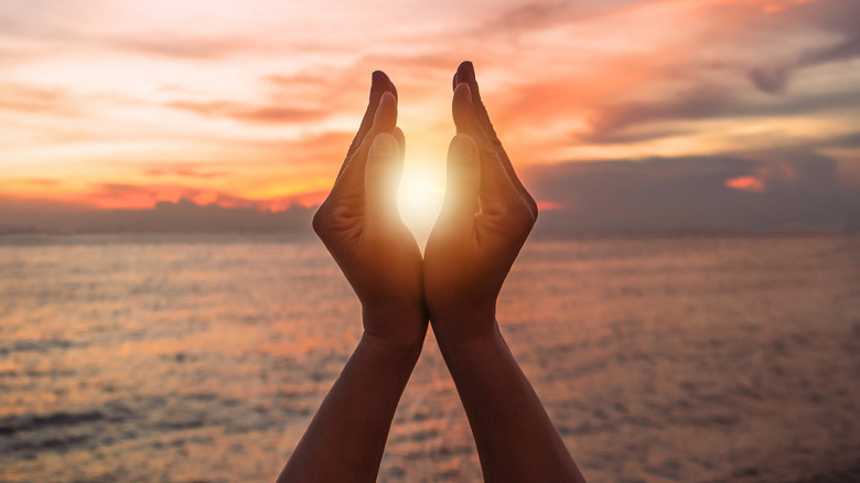 Woman using cupping motion with hands around sun that is in the distance