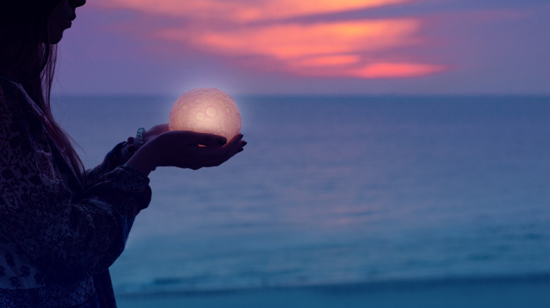person holding moon in hands on beach by water