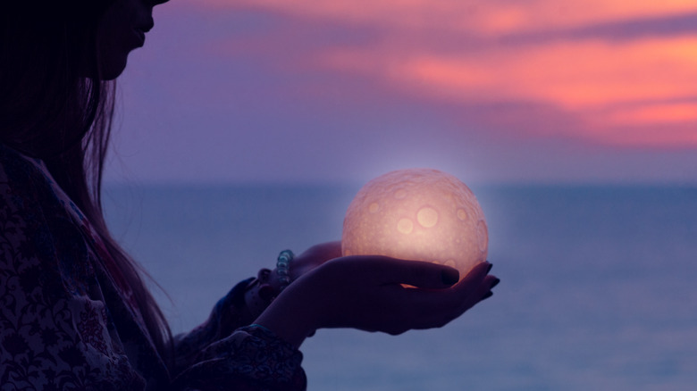 Woman cupping a moon over the ocean