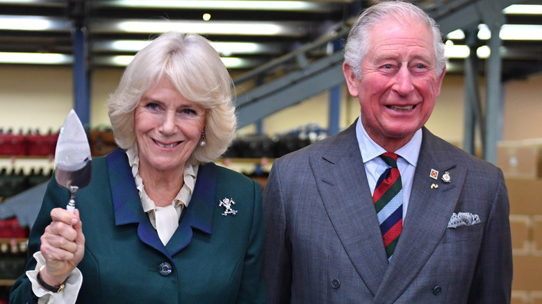 Queen consort Camilla holding up a cake server and King Charles III smiling