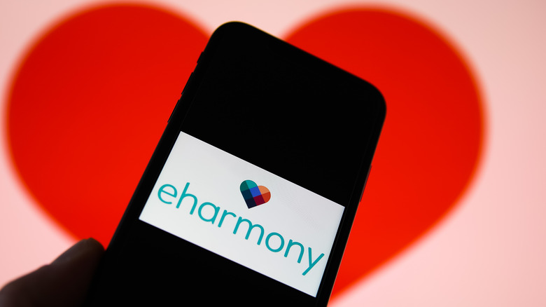 Cell phone with eharmony logo on screen and a red heart in background