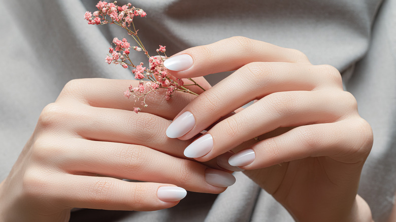 Closeup of woman's fingernails while she holds a pink flower