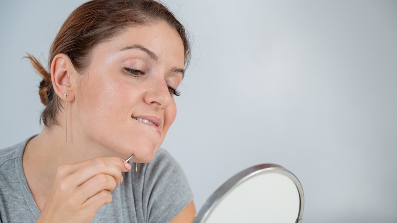 Woman plucking chin hair in mirror