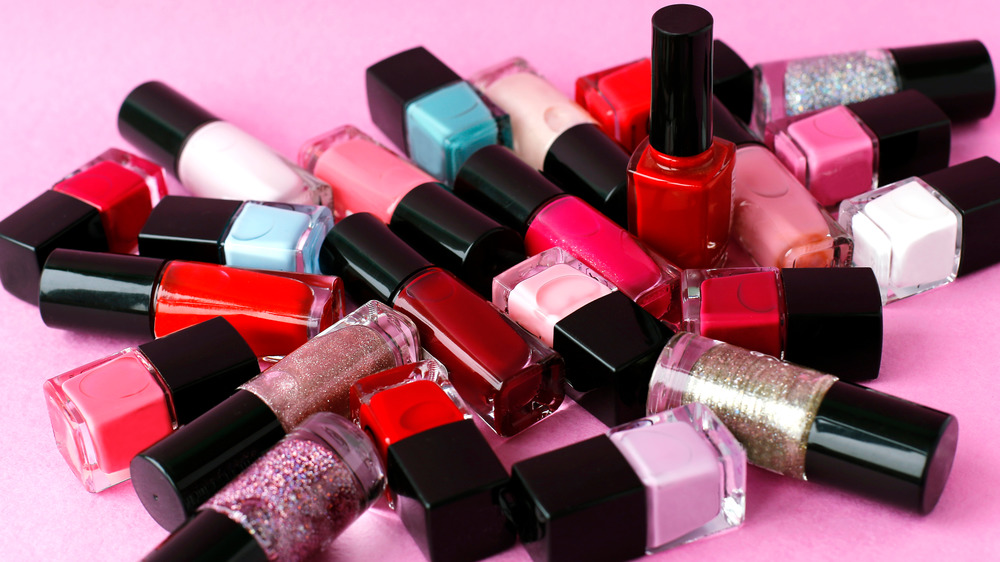 Several bottles of nail polish in a pile on a pink background.