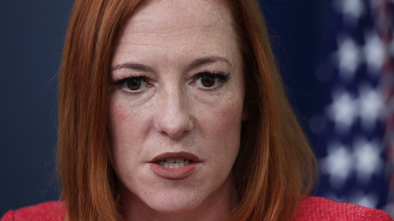 Jen Psaki wearing a red suit in the White House briefing room