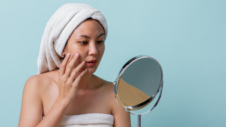 A woman touching the side of her face while looking at the mirror.