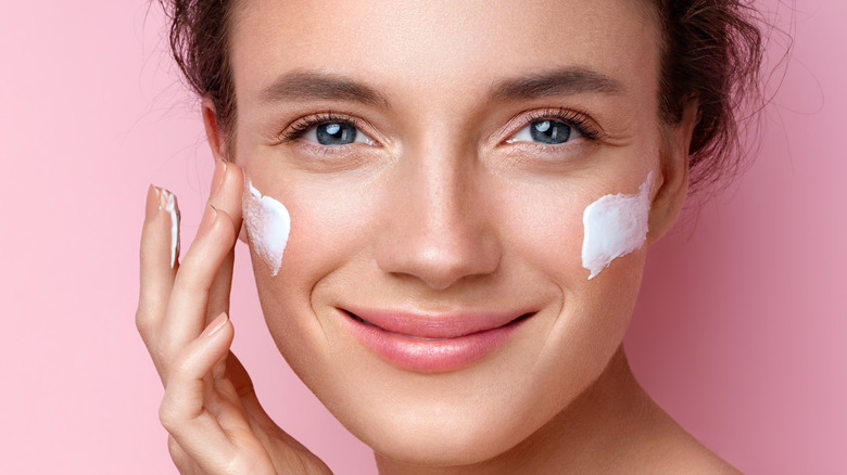 Woman applies moisturizer to her face