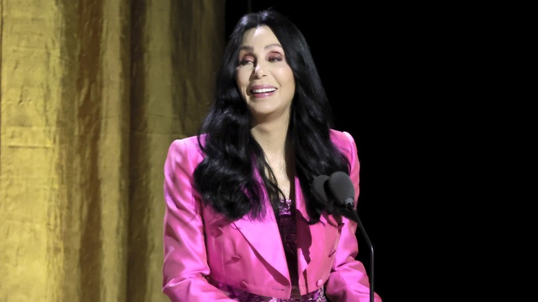 Cher smiling at podium in a hot pink jacket