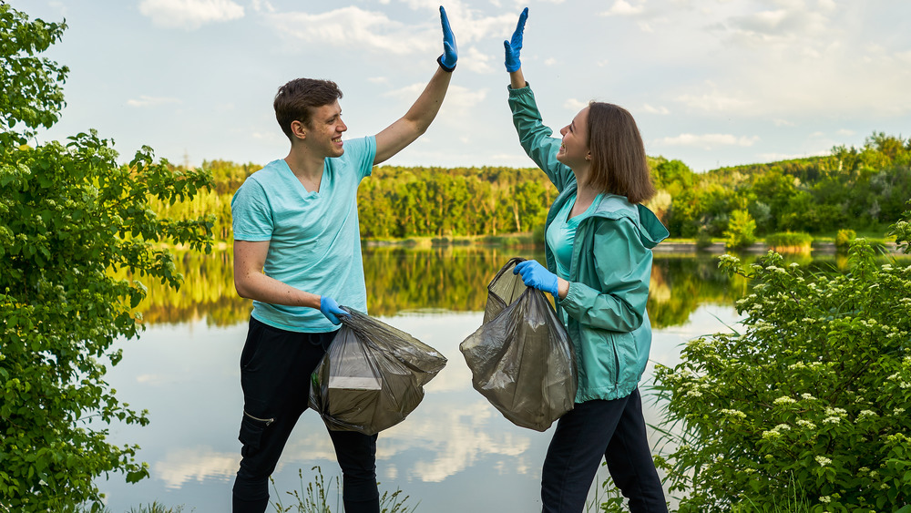 A man and woman high-five while holding trash bags 