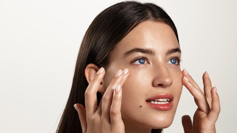 A woman touches the skin under her eyes. 