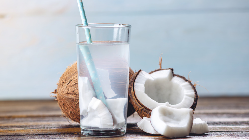 Glass of coconut water with coconut pieces in it