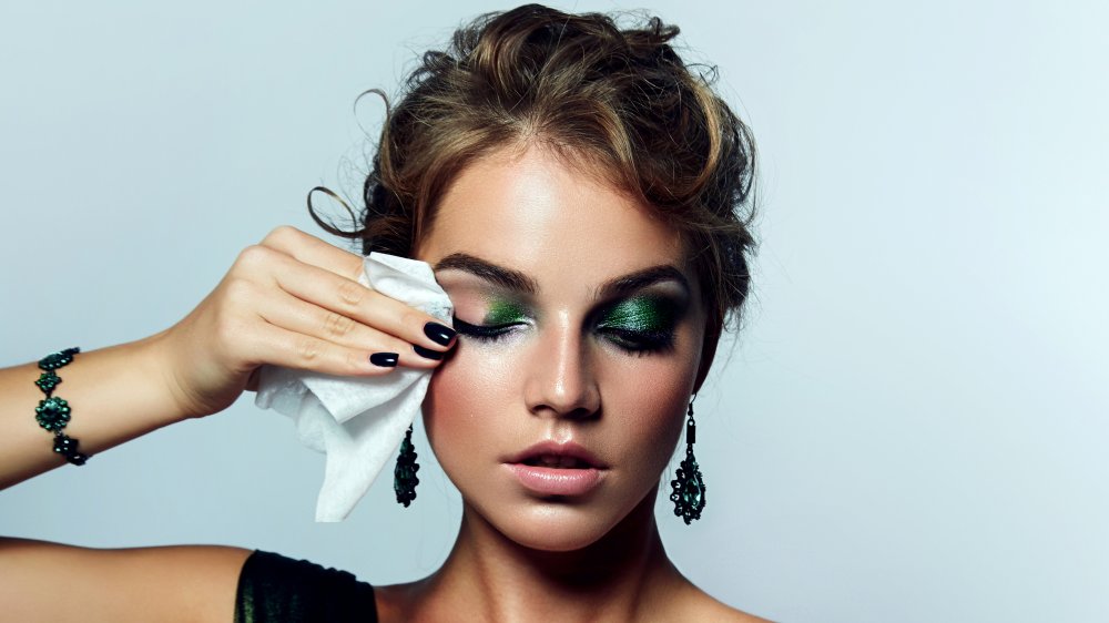 Woman using makeup remover wipe on green eye shadow