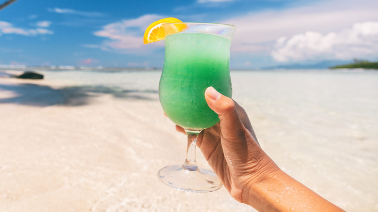 Hand holding up green drink on the beach