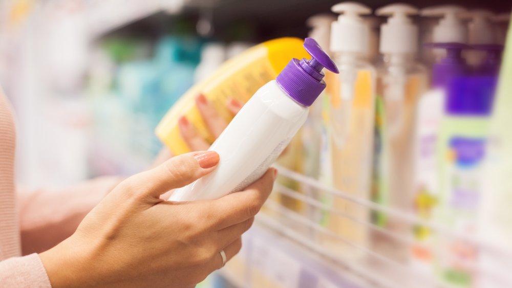 A hand selecting a bottle of lotion from a shelf 