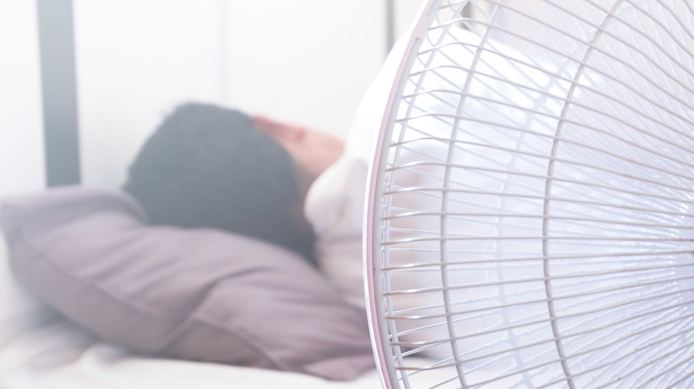 Person sleeping with a fan nearby