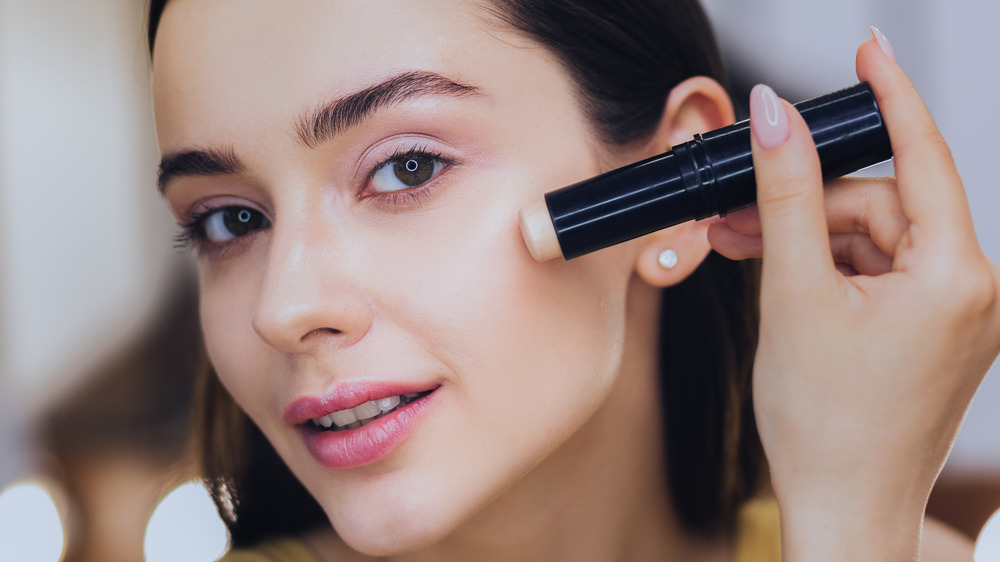 Woman applying stick foundation to face