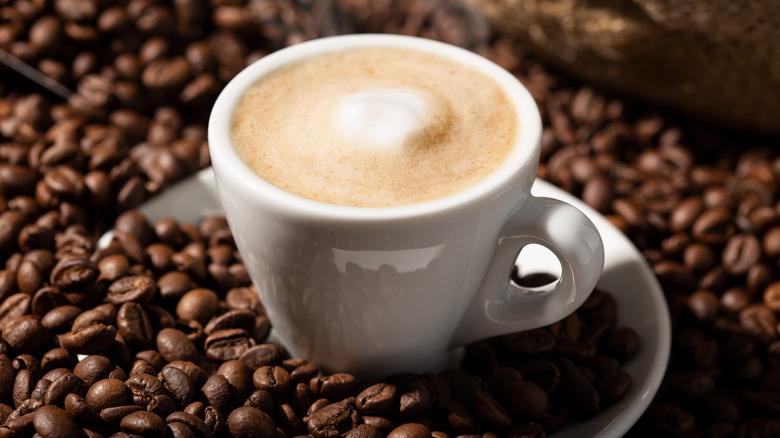 White mug full of coffee surrounded by brown coffee beans.